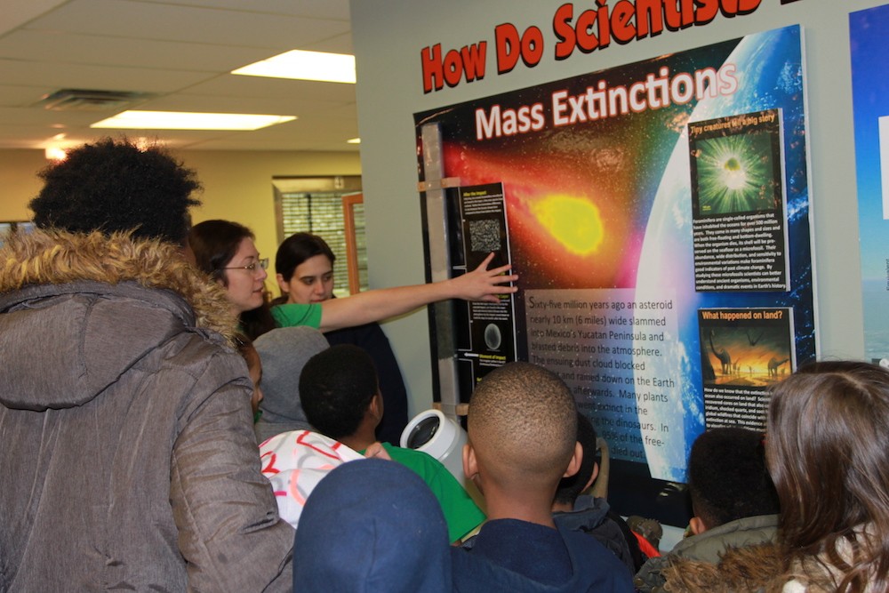 Curator Nichole Anest explains how a series of sediment cores provide evidence for the impact theory of the mass extinction ~65 million years ago. Core Repository curator explains a poster on mass extinction to a group of attendees