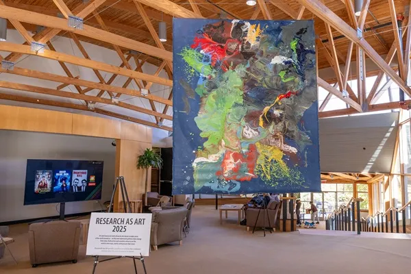 Large "paint pour" mural hanging from ceiling of Monell Building lobby with Research as Art 2025 sign in the foreground.